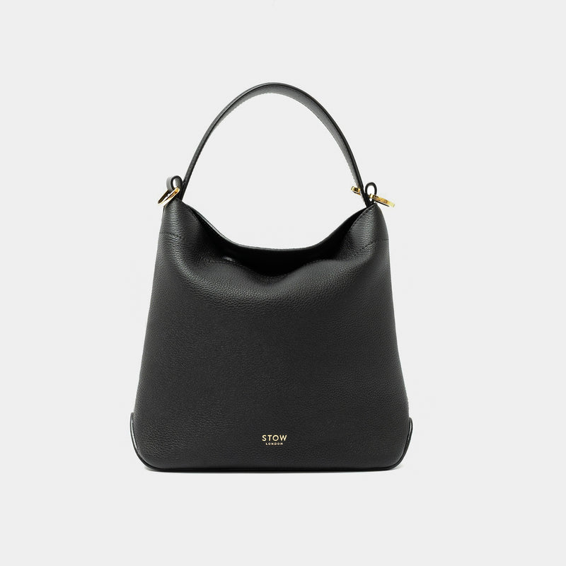 STOW London's Midi Curve in Black pebbled leather styled as a flap bag featuring gold-coated stainless steel hardware on a light grey background