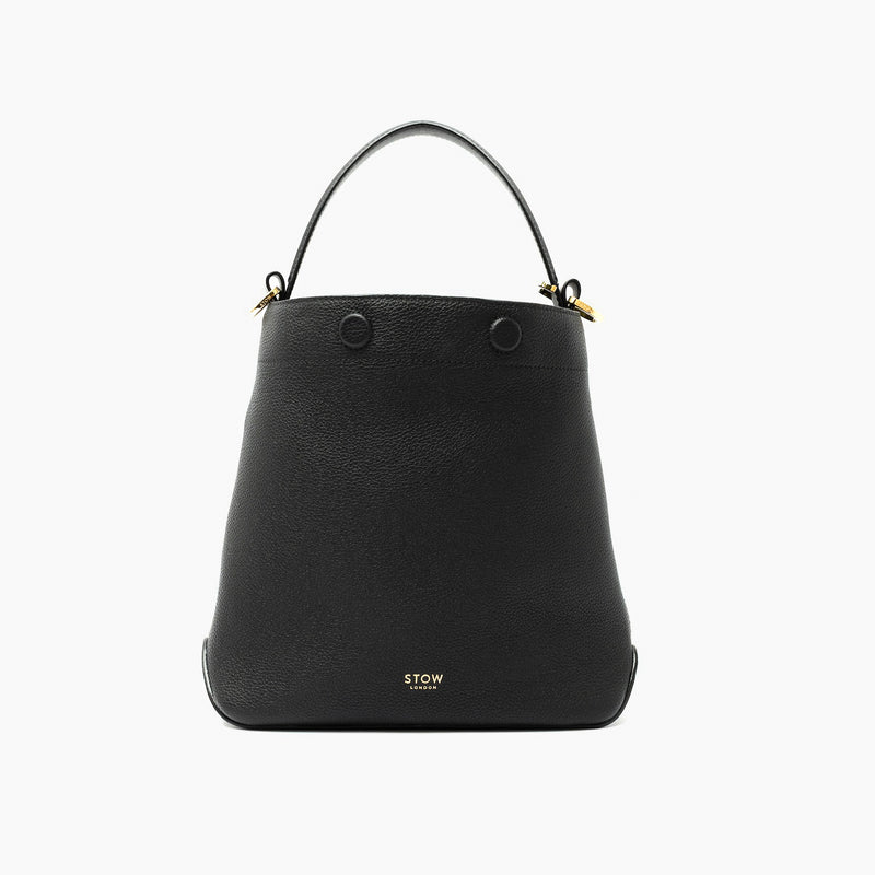 STOW London's Midi Curve in Black pebbled leather styled as a bucket bag featuring gold-coated stainless steel hardware on a light grey background