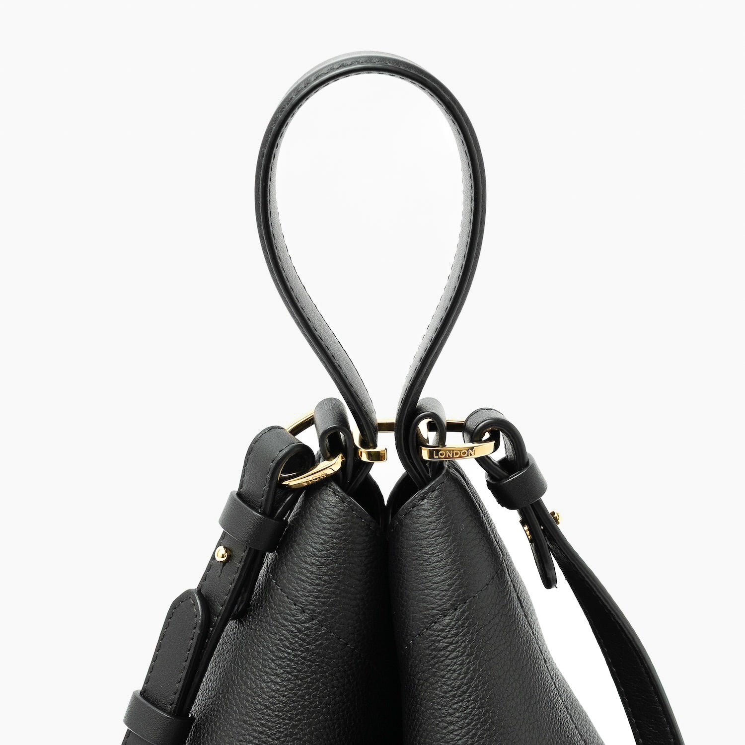 Close up of the handles on STOW London's Midi Curve in Black pebbled leather featuring gold-coated stainless steel hardware, clip and detachable on a light grey background