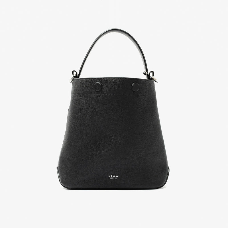 STOW London's Midi Curve in Black pebbled leather styled as a bucket bag featuring silver stainless steel hardware on a light grey background