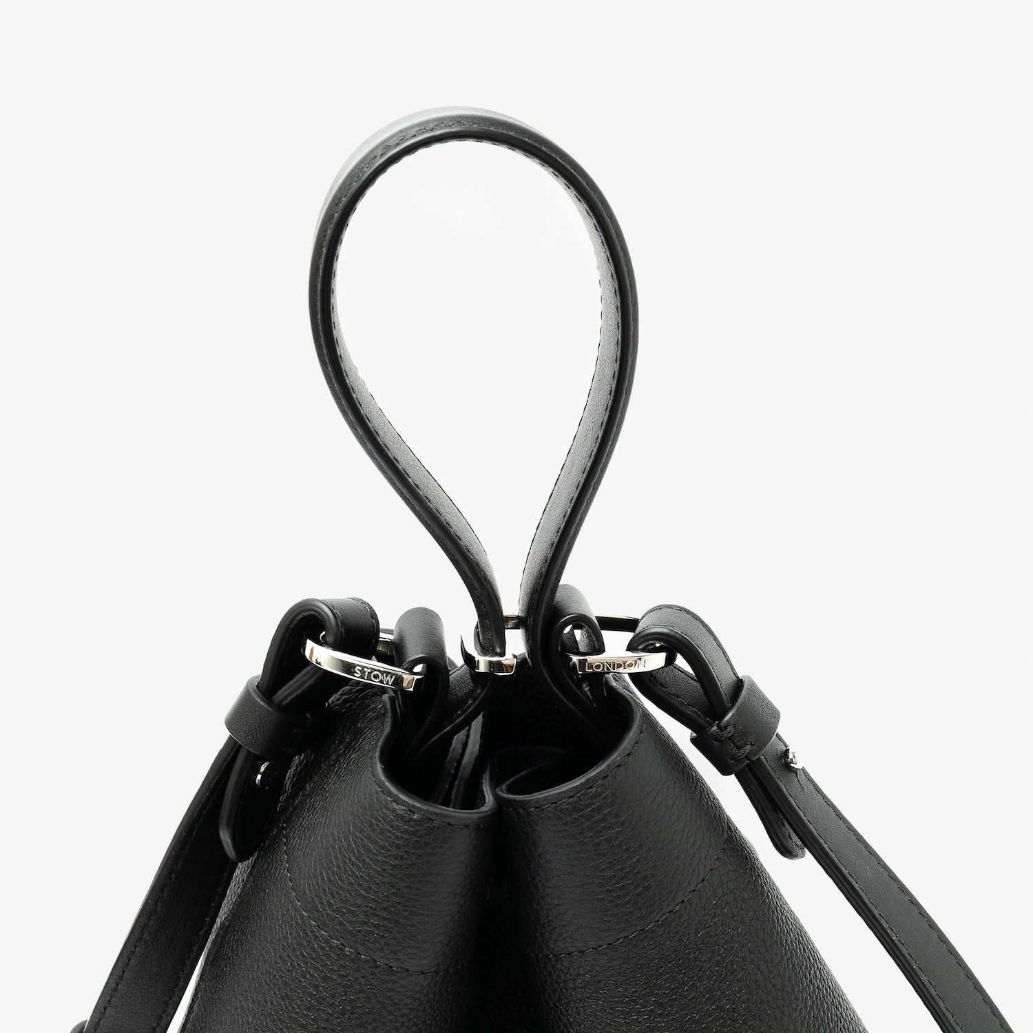 Close up of the handles on STOW London's Midi Curve in Black pebbled leather featuring silver stainless steel hardware, clip and detachable strap on a light grey background