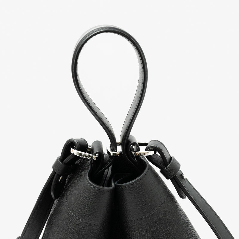 Close up of the handles on STOW London's Midi Curve in Black pebbled leather featuring silver stainless steel hardware, clip and detachable strap on a light grey background