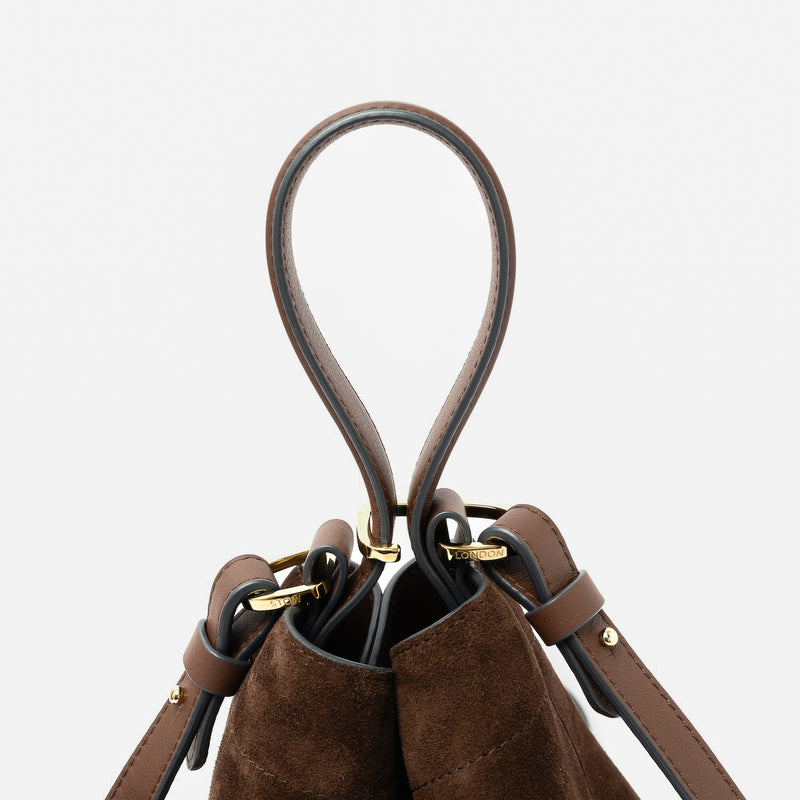 Close up of the handles of STOW London's Midi Curve in Chocolate suede leather featuring gold-coated stainless steel hardware, clip and detachable strap on a light grey background