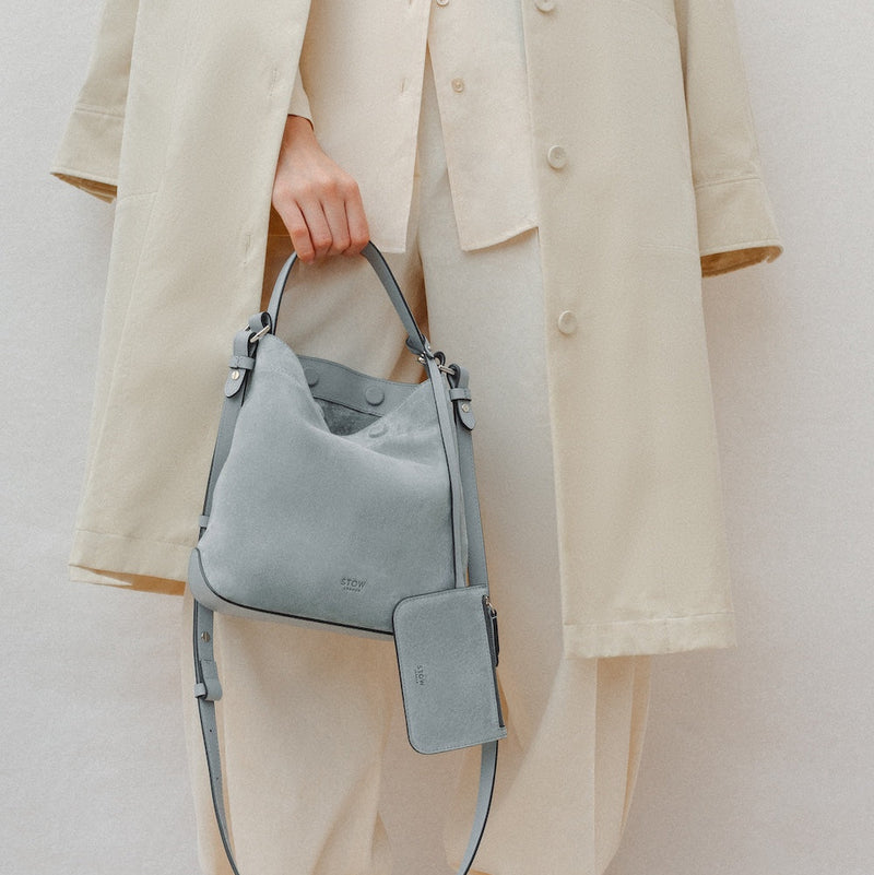 Model holding STOW London's Midi Curve in Misty Blue suede leather featuring silver stainless steel hardware