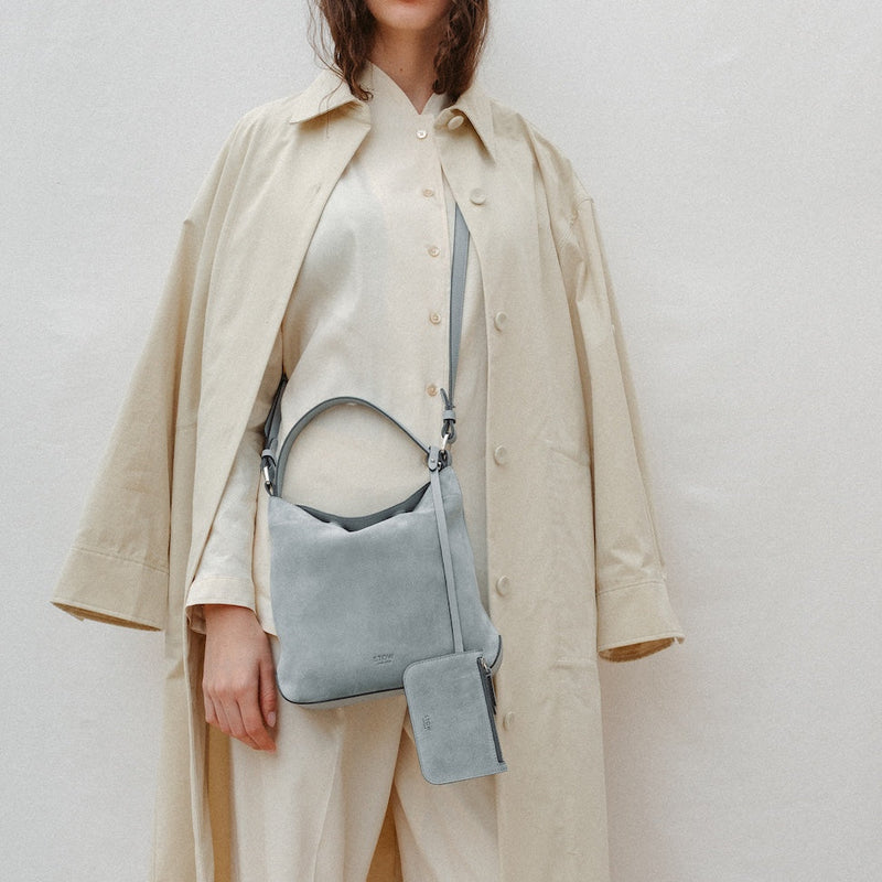 Model wearing STOW London's Midi Curve in Misty Blue suede leather crossbody featuring silver stainless steel hardware