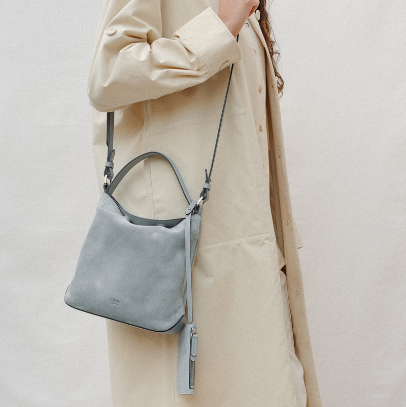 Model wearing STOW London's Midi Curve in Misty Blue suede leather on her shoulder featuring silver stainless steel hardware