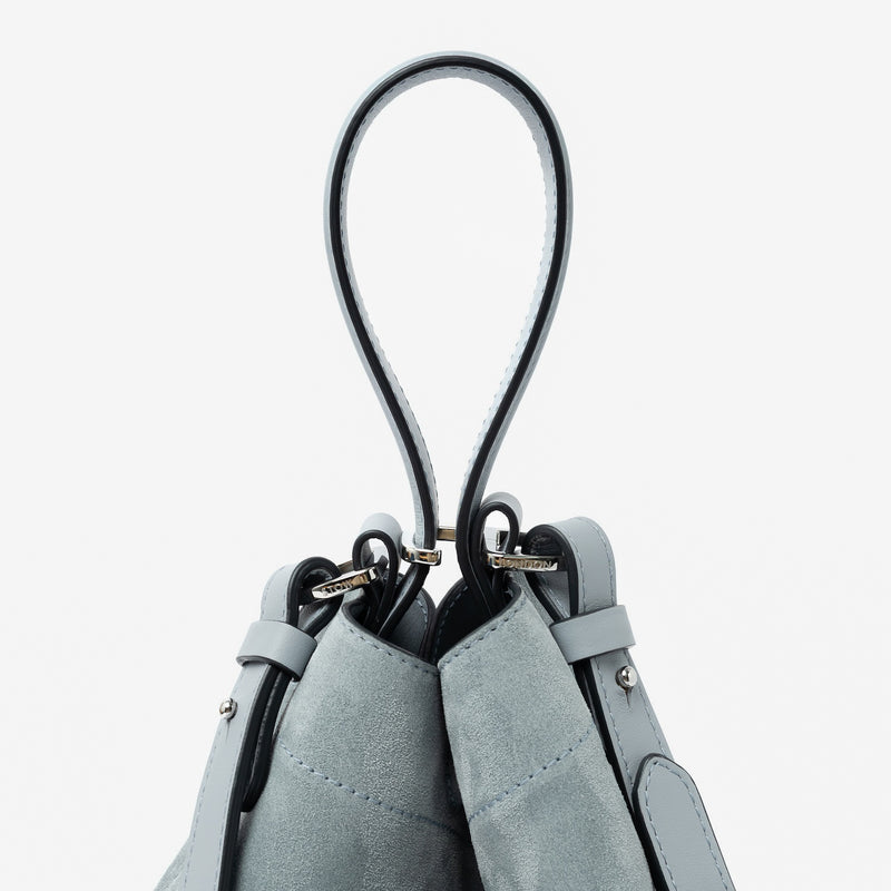 Close up of the handle on STOW London's Midi Curve in Misty Blue suede leather featuring silver stainless steel hardware, clip and detachable crossbody strap on a light grey background