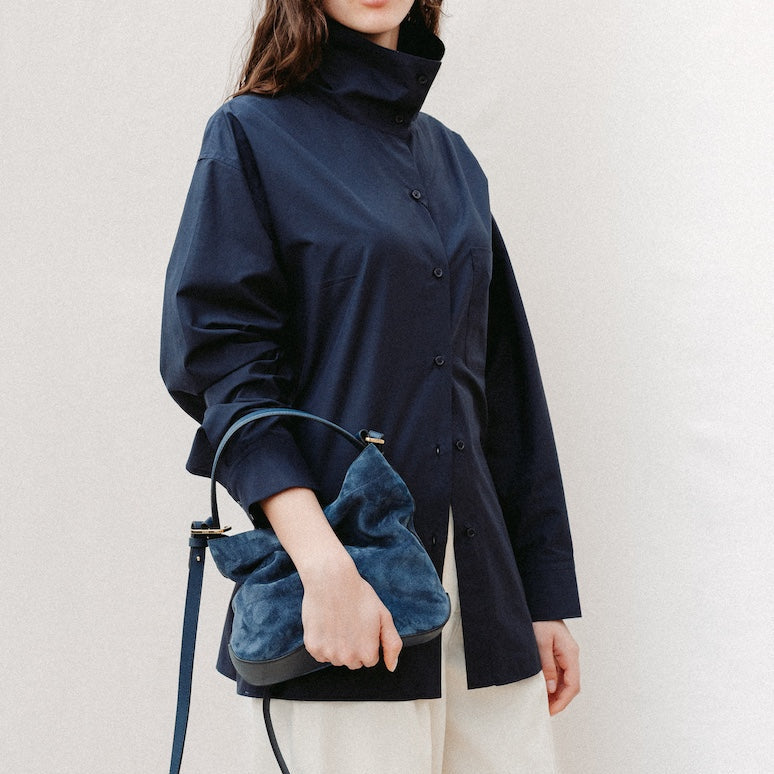 Model holding STOW London's Midi Curve in Navy suede leather featuring gold-coated stainless steel hardware