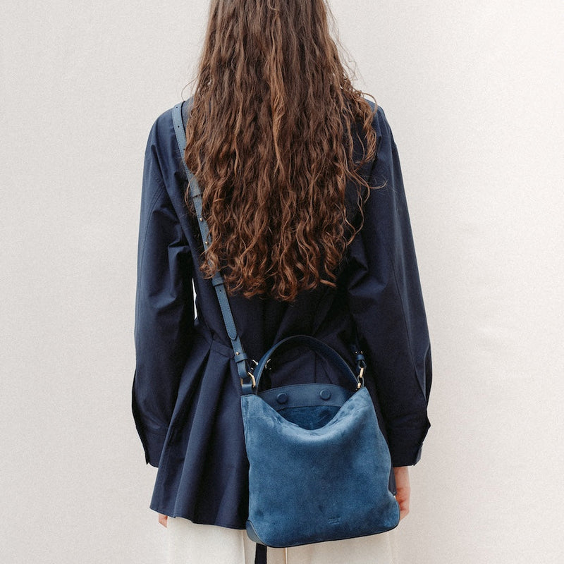 Model wearing STOW London's Midi Curve in Navy suede leather crossbody featuring gold-coated stainless steel hardware