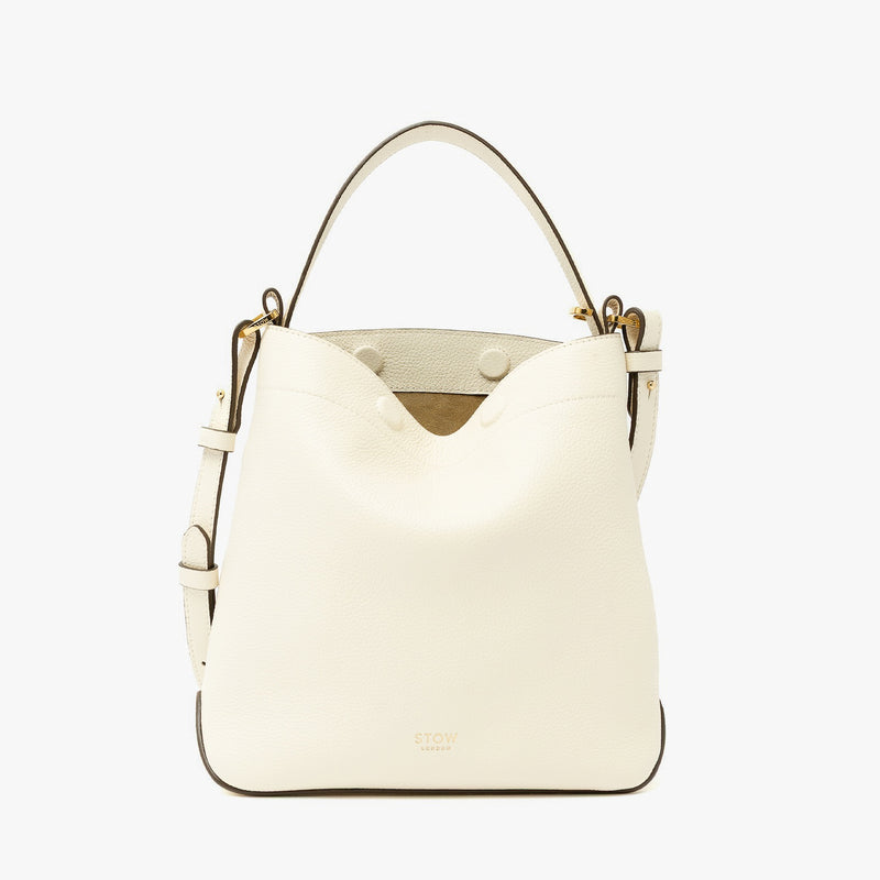 STOW London's Midi Curve in Spring Moon pebbled leather and detachable crossbody strap featuring gold-coated stainless steel hardware on a light grey background