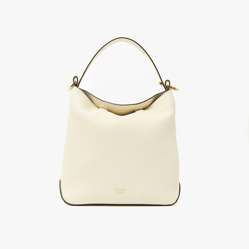 STOW London's Midi Curve in Spring Moon pebbled leather shaped as flap bag featuring gold-coated stainless steel hardware on a light grey background