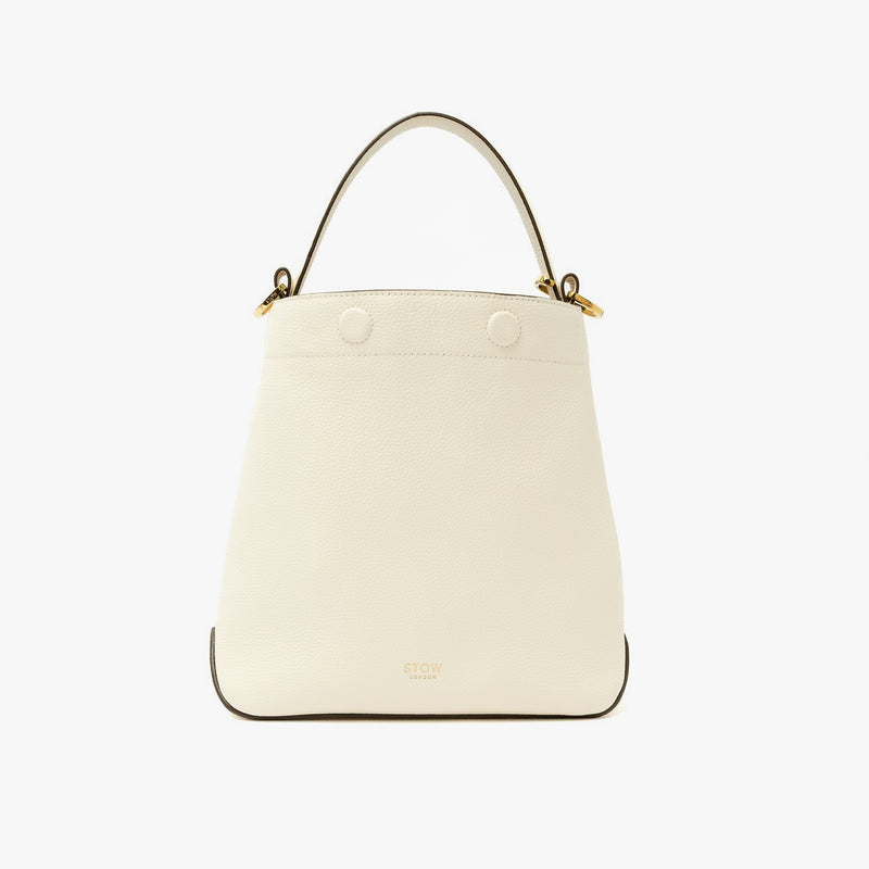 STOW London's Midi Curve in Spring Moon pebbled leather styled as a bucket bag featuring gold-coated stainless steel hardware on a light grey background