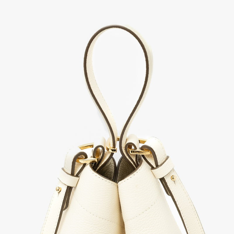 Close up of the handles on STOW London's Midi Curve in Spring Moon pebbled leather featuring gold-coated stainless steel hardware, clip and detachable strap on a light grey background