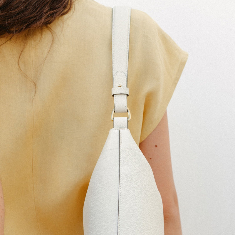 Model wearing STOW London's Midi Curve in Spring Moon leather on her shoulder featuring the detachable shoulder strap with gold hardware and details 
