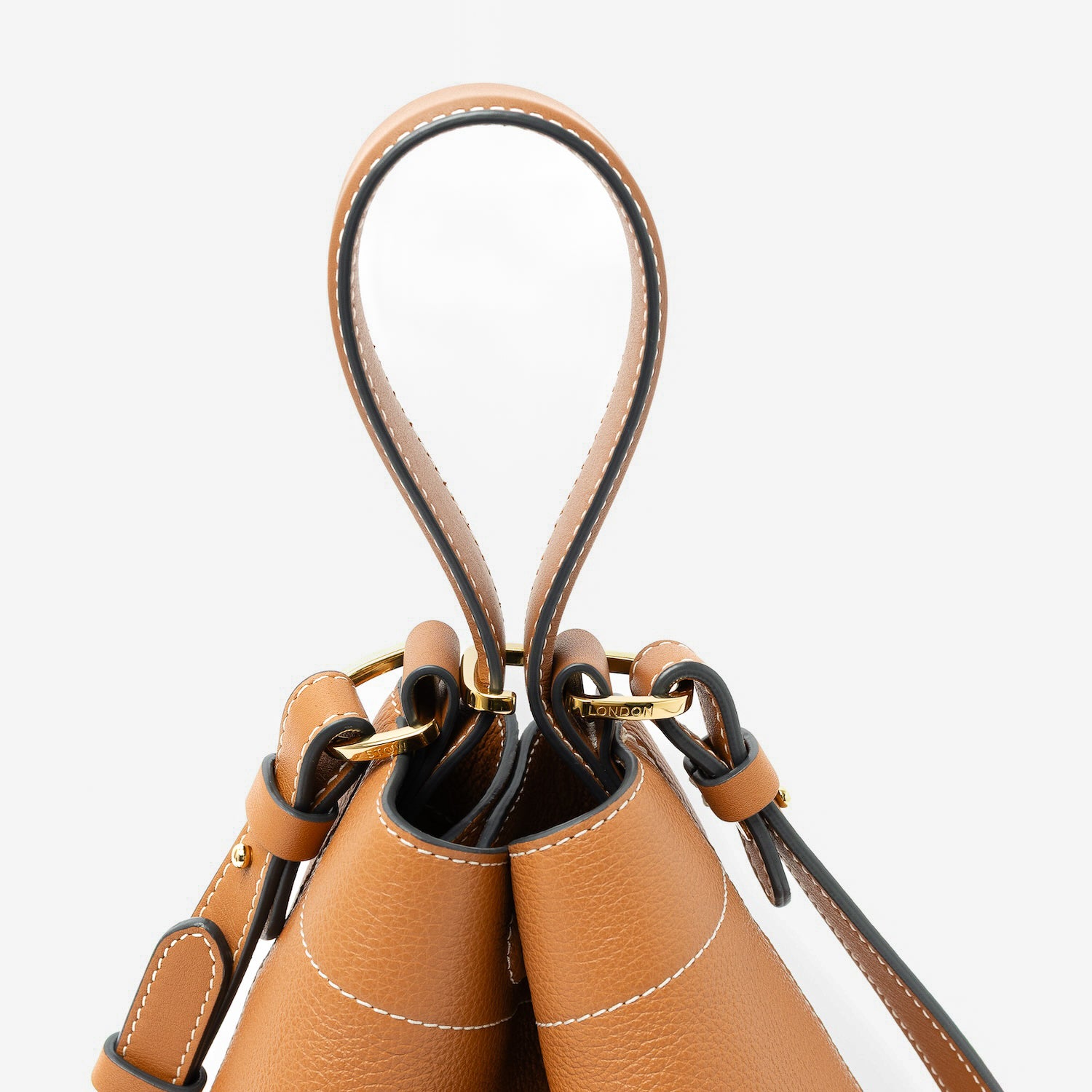 Close up of the handles on STOW London's Midi Curve in Earth Tan pebbled leather featuring gold-coated stainless steel hardware, clip and detachable strap on a light grey background