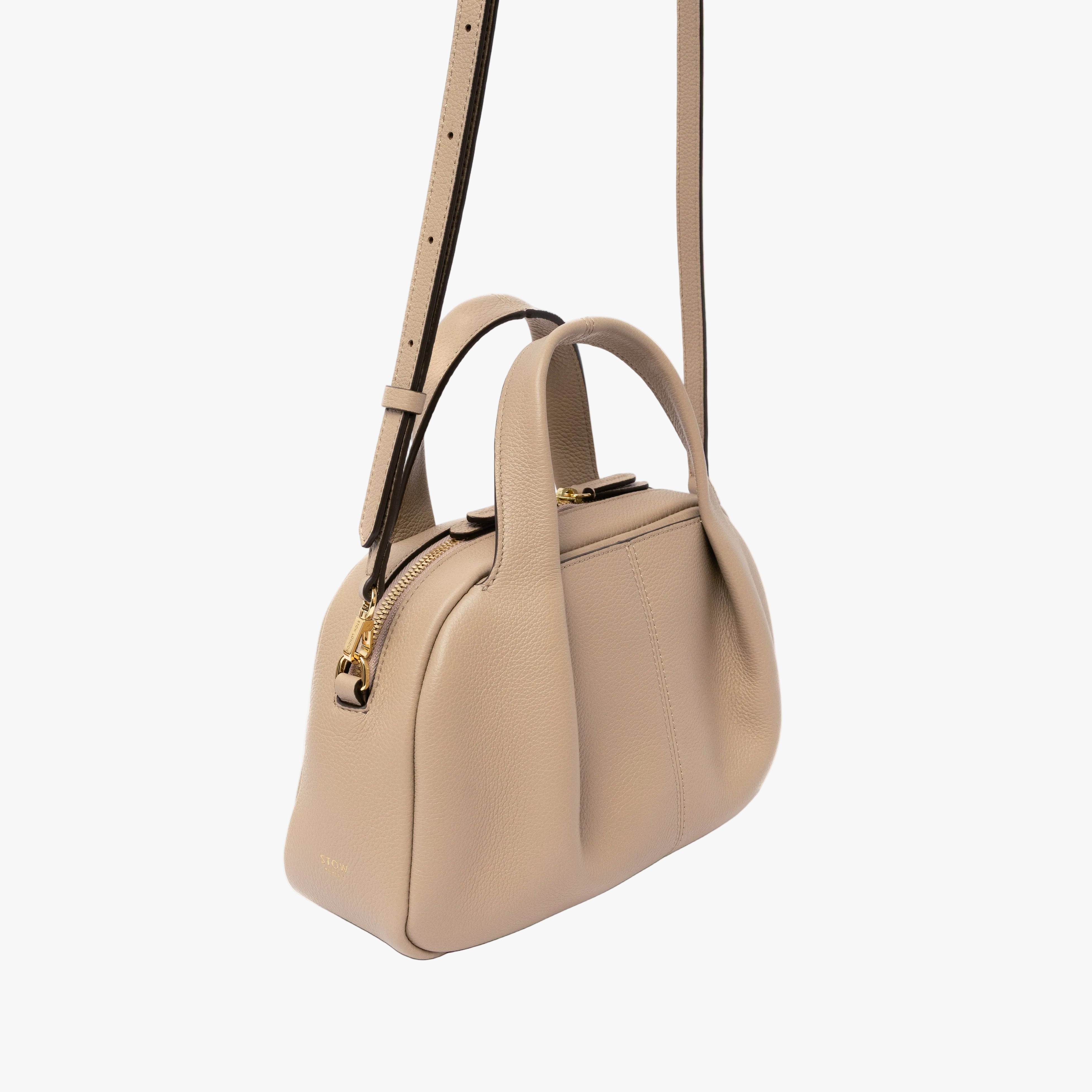 STOW London's Mini Bowling in Camel pebbled leather featuring a pleated front panel and gold-coated stainless steel hardware on a light grey background