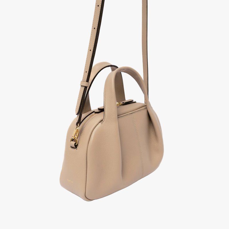 STOW London's Mini Bowling in Camel pebbled leather featuring a pleated front panel and gold-coated stainless steel hardware on a light grey background