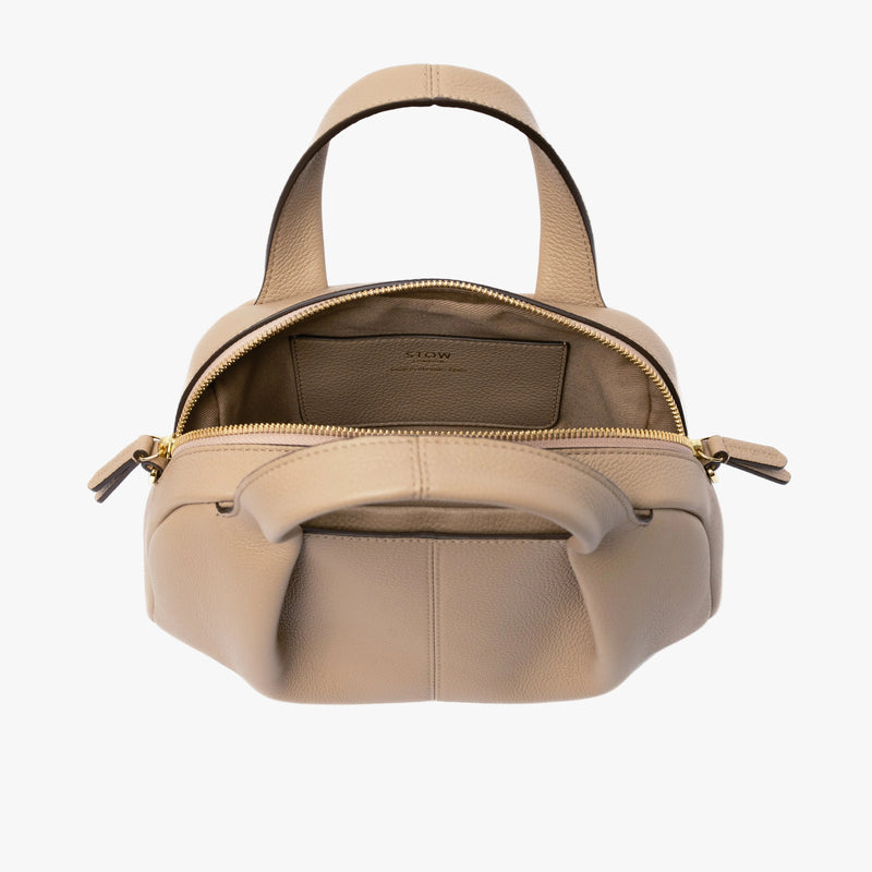 STOW London's Mini Bowling in Camel pebbled leather with zips open showing the cotton interior lining and leather slip pocket featuring gold-coated stainless steel hardware on a light grey background