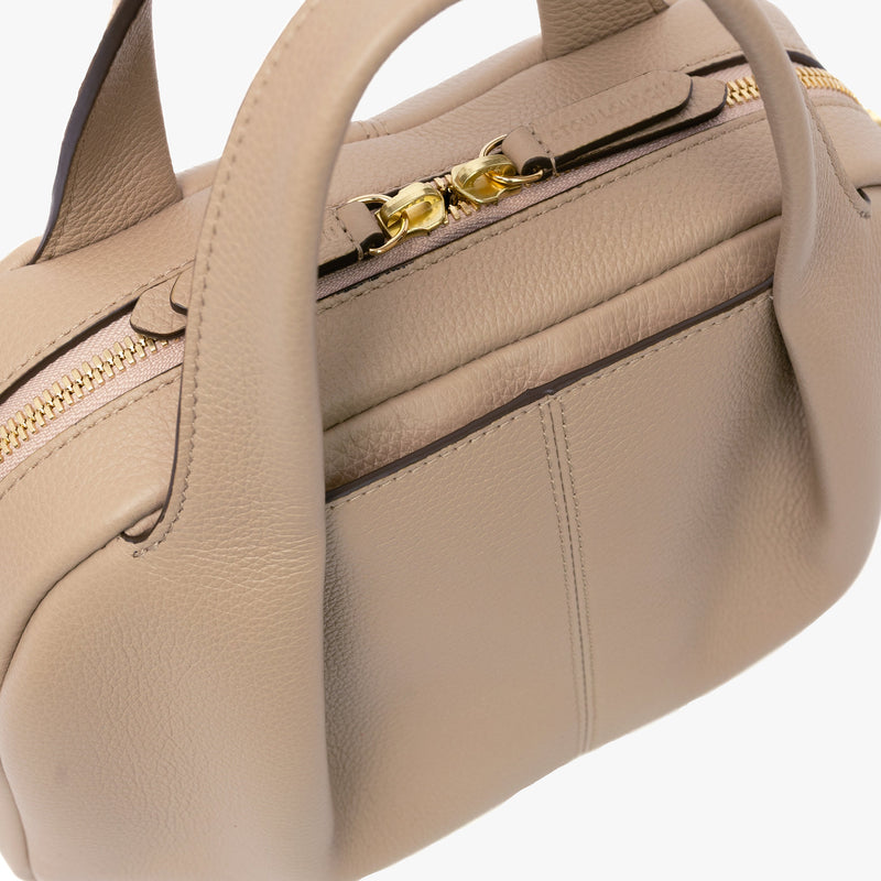 Close up of STOW London's Mini Bowling in Camel pebbled leather featuring a pleated front panel and gold-coated stainless steel hardware on a light grey background