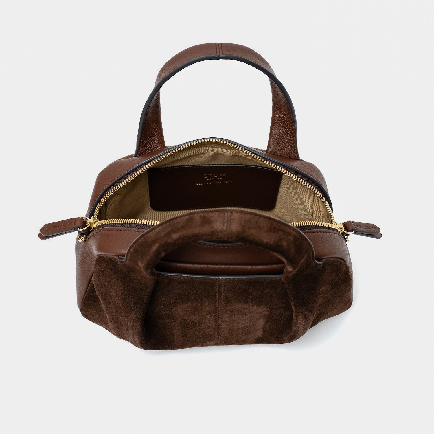 STOW London's Mini Bowling bag in Chocolate suede and smooth leather with zips open showing light beige interior lining and slip pocket featuring gold-coated stainless steel hardware on a light grey background