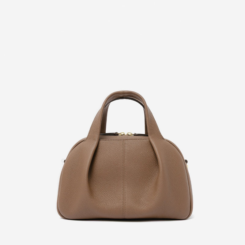 STOW London's Mini Bowling bag in Mocha pebbled leather featuring a pleated front panel and gold-coated stainless steel hardware on a light grey background