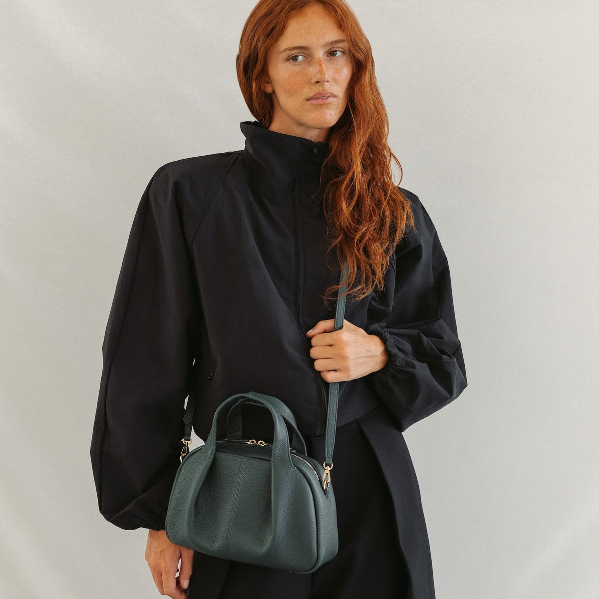 Model wearing STOW London's Mini Bowling in New Forest pebbled leather crossbody featuring a pleated front panel and gold-coated stainless steel hardware 
