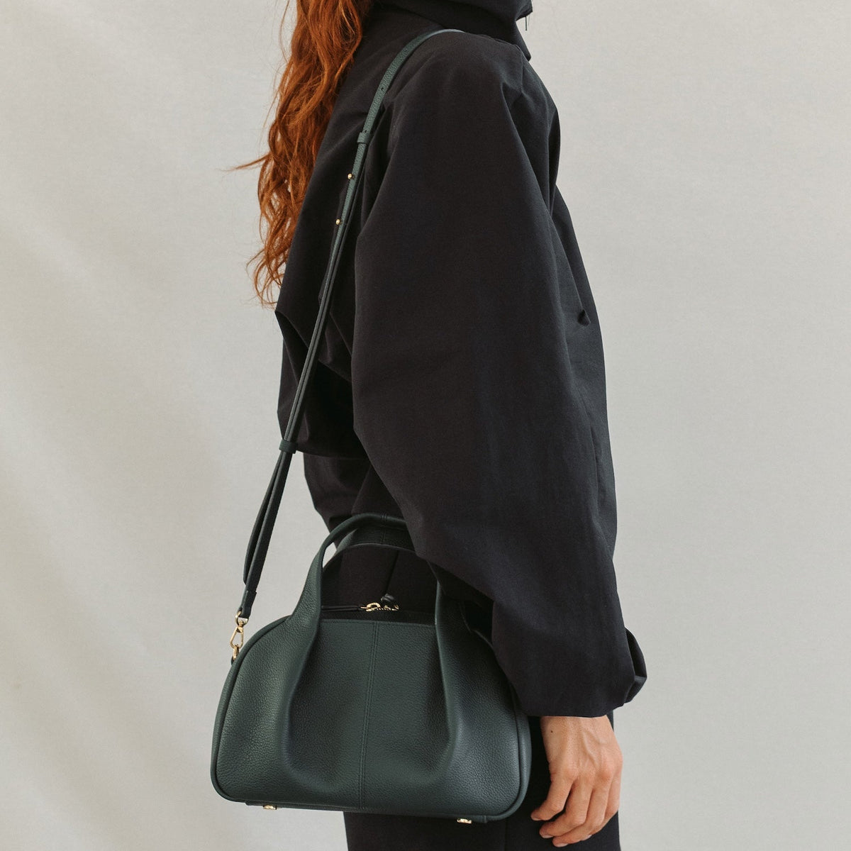 Model wearing STOW London's Mini Bowling in New Forest pebbled leather crossbody featuring a pleated front panel and gold-coated stainless steel hardware 