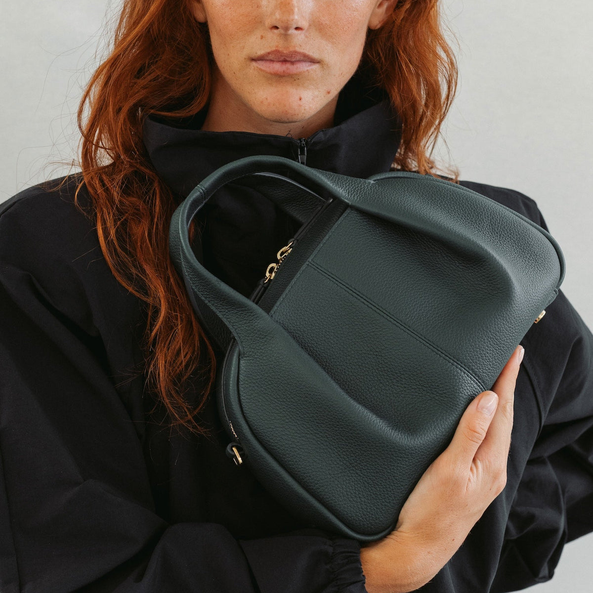 Model holding STOW London's Mini Bowling in New Forest pebbled leather featuring a pleated front panel and gold-coated stainless steel hardware 