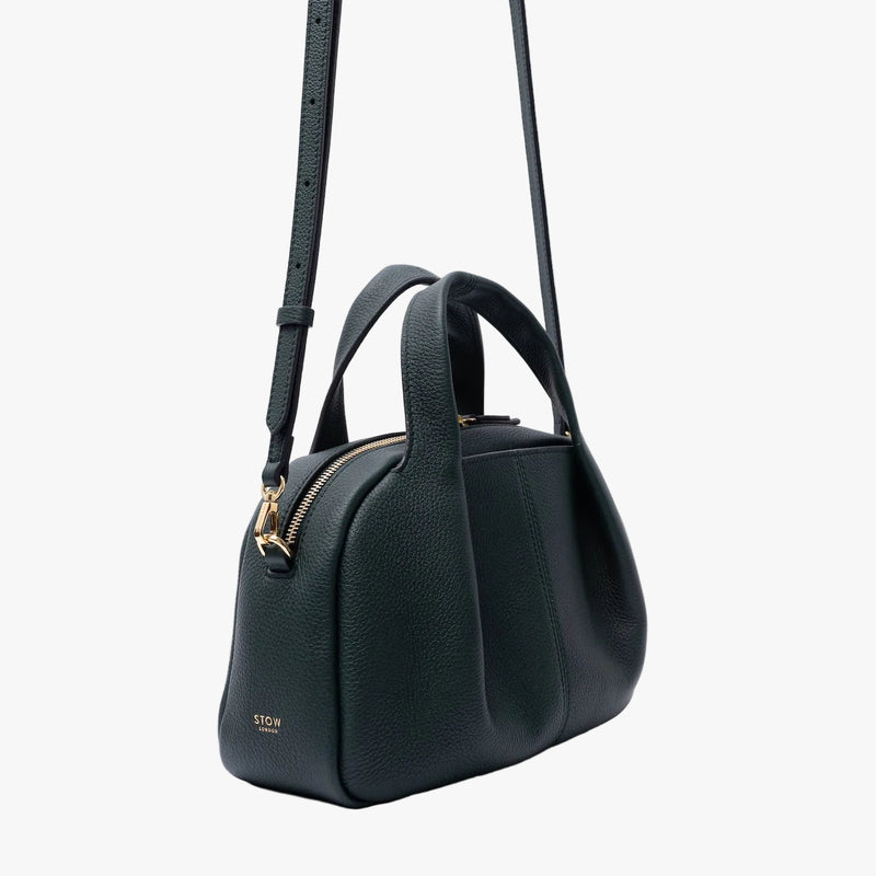Off-axis view of STOW London's Mini Bowling in New Forest pebbled leather on a light grey background featuring gold-coated stainless steel hardware and the detachable crossbody strap
