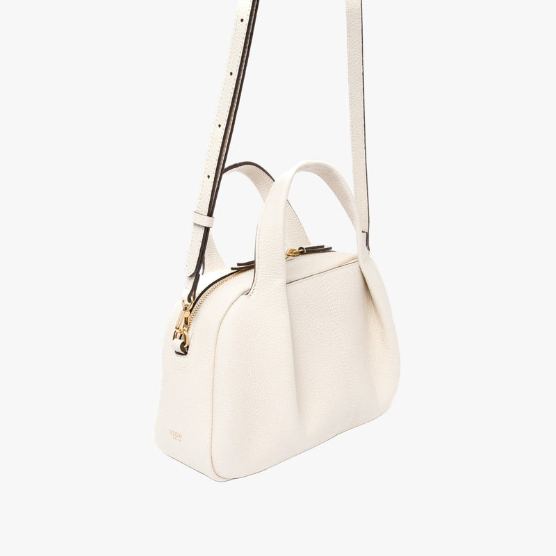Off-axis view of STOW London's Mini Bowling bag in Spring Moon pebbled leather featuring a pleated front panel and gold-coated stainless steel hardware on a light grey background