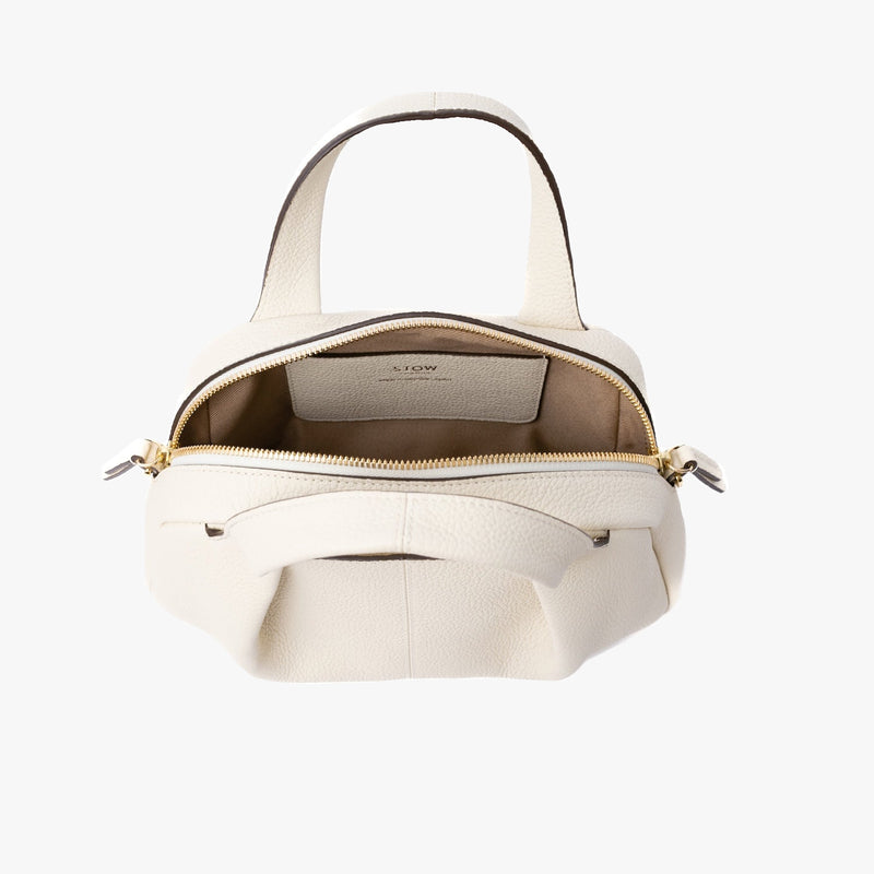STOW London's Mini Bowling bag in Spring Moon pebbled leather with zip open showing cotton interior lining and leather slip pocket featuring gold-coated stainless steel hardware on a light grey background