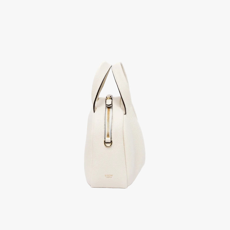 Side view of STOW London's Mini Bowling bag in Spring Moon pebbled leather featuring gold-coated stainless steel hardware on a light grey background
