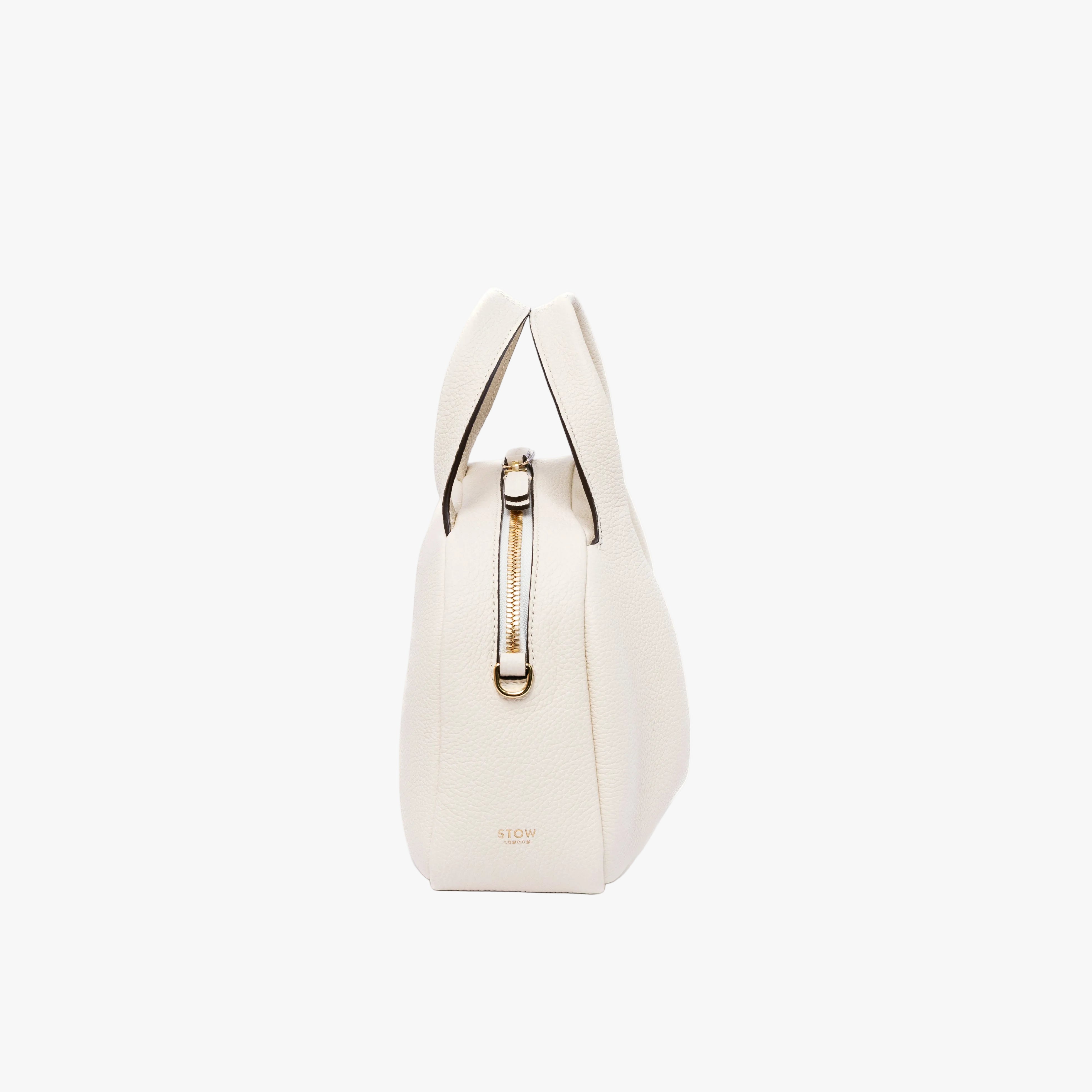 Side view of STOW London's Mini Bowling bag in Spring Moon pebbled leather featuring gold-coated stainless steel hardware on a light grey background