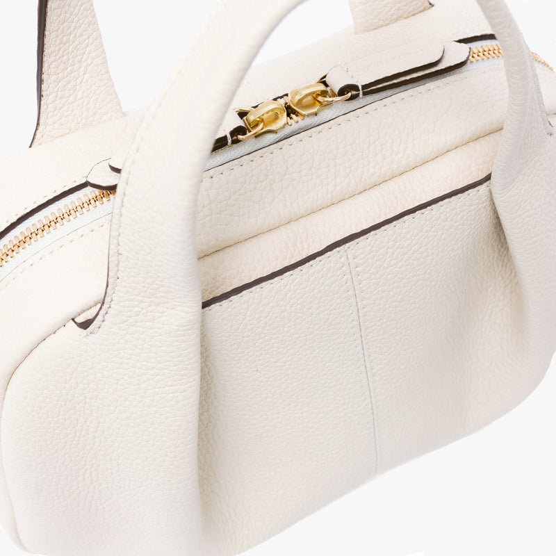Close up of STOW London's Mini Bowling bag in Spring Moon pebbled leather featuring a pleated front panel and gold-coated stainless steel hardware on a light grey background