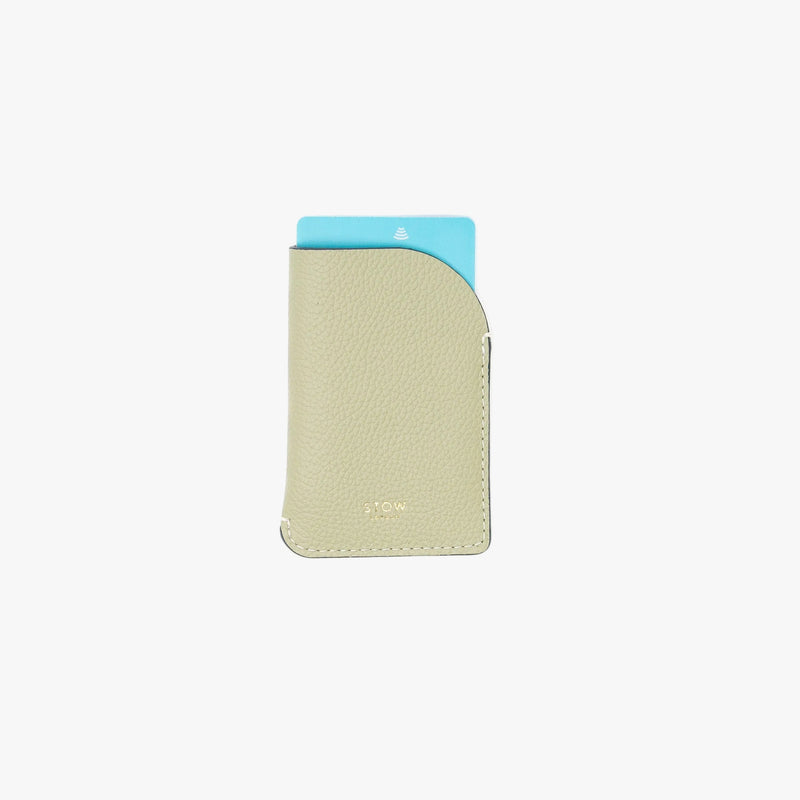 STOW London's Mini Cardholder in Pale Green pebbled leather on a light grey background featuring a card sticking out the top and a small gold embossed logo on the front bottom