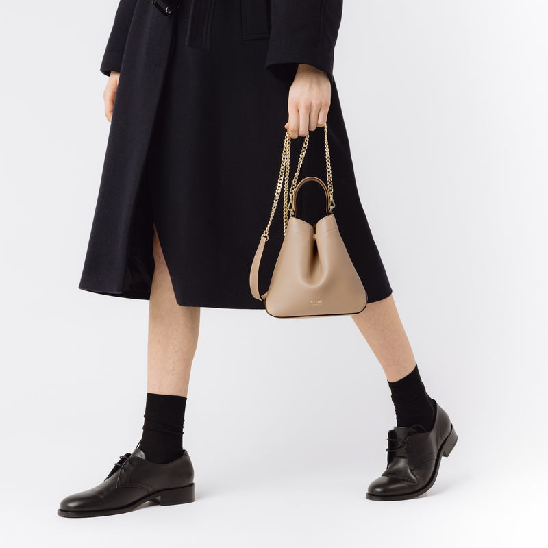 Model with STOW London's Mini Curve in Camel leather featuring the gold-plated chain on a white background