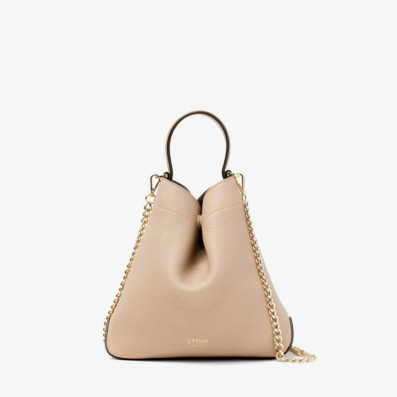 Stow London's Mini Curve in Camel pebbled leather and detachable gold chain crossbody strap on a light grey background 