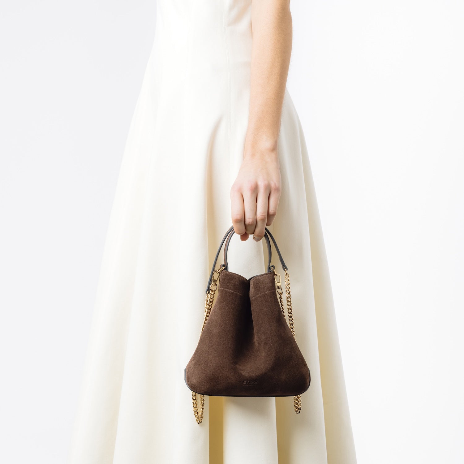 Model holding STOW London's Mini Curve in Chocolate suede leather at her side featuring the detachable crossbody gold plated chain