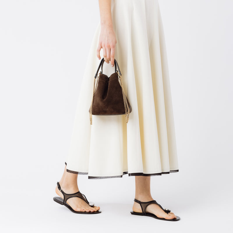 Model holding STOW London's Mini Curve in Chocolate suede leather at her side featuring gold-coated stainless steel hardware
