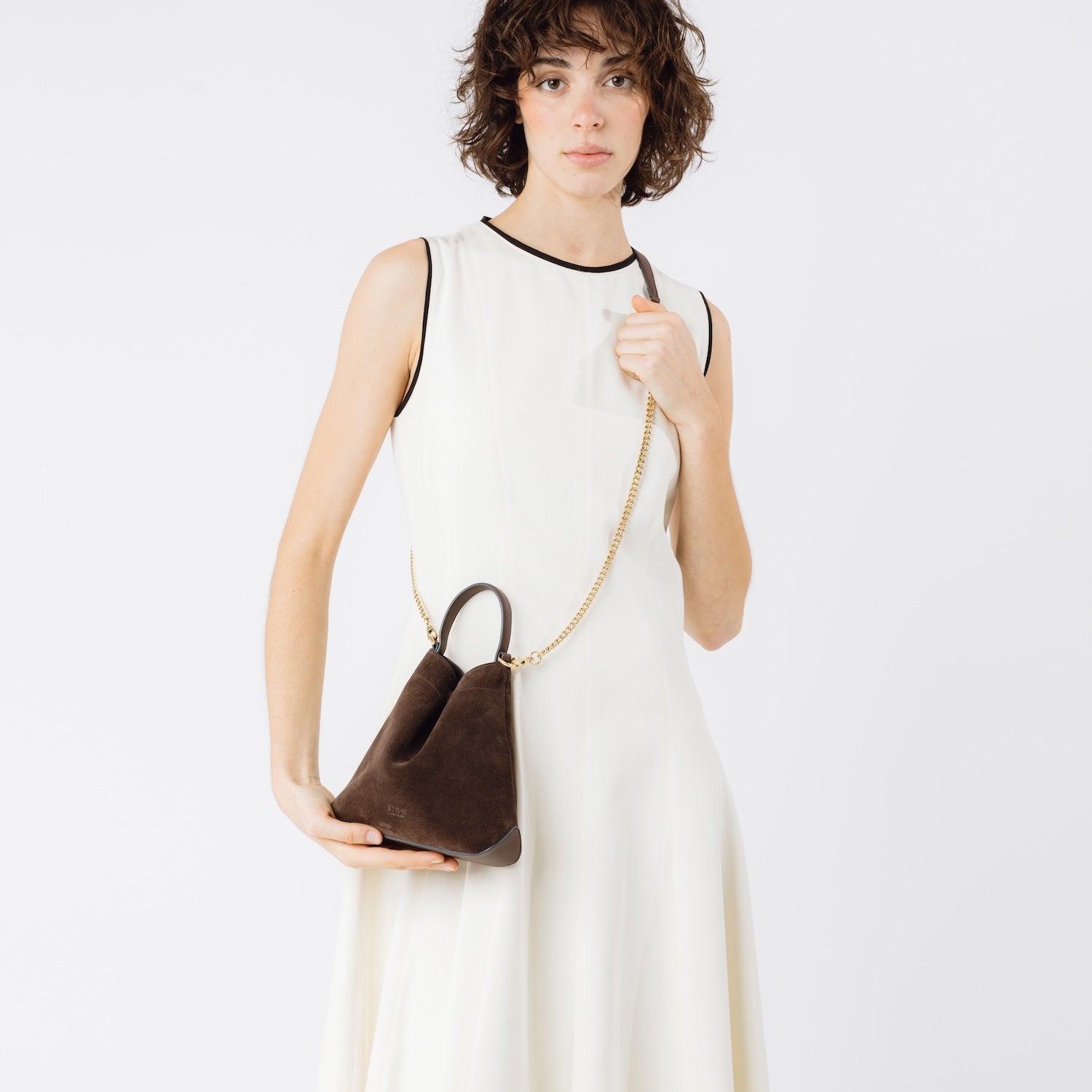 Model wearing STOW London's Mini Curve in Chocolate suede leather crossbody featuring gold-coated stainless steel hardware