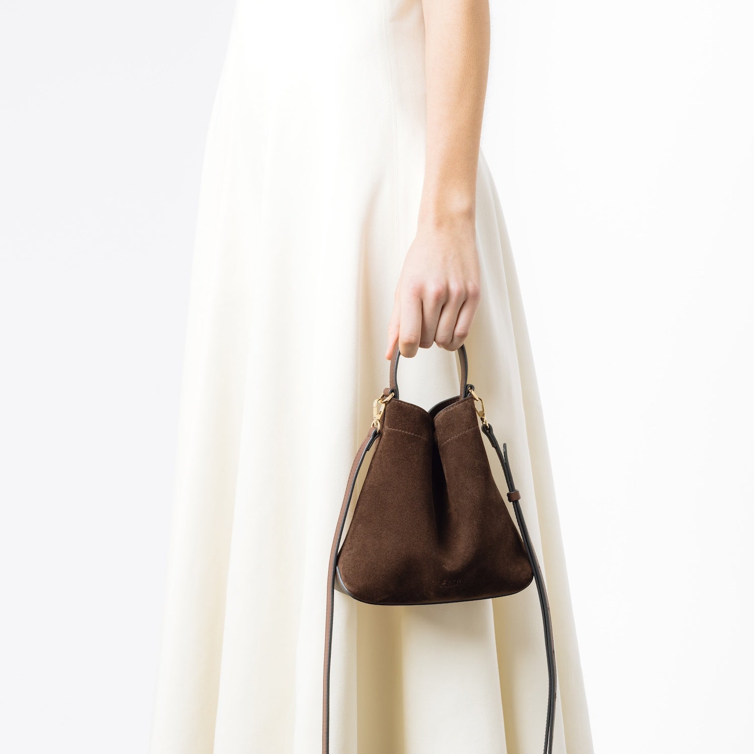 Model holding STOW London's Mini Curve in Chocolate suede leather featuring its detachable crossbody full leather strap