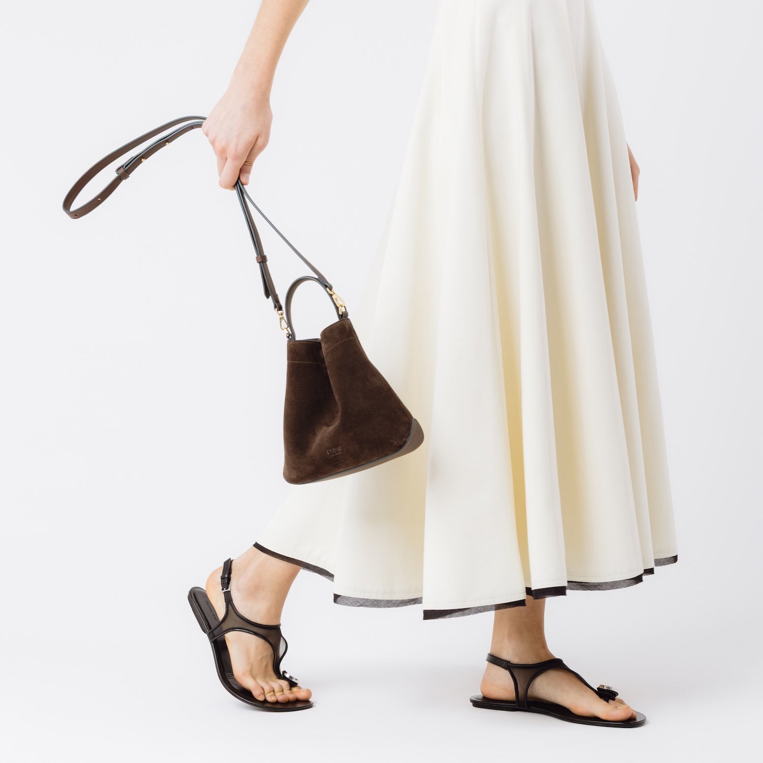 Model holding STOW London's Mini Curve in Chocolate suede leather at her side featuring its detachable crossbody full leather strap