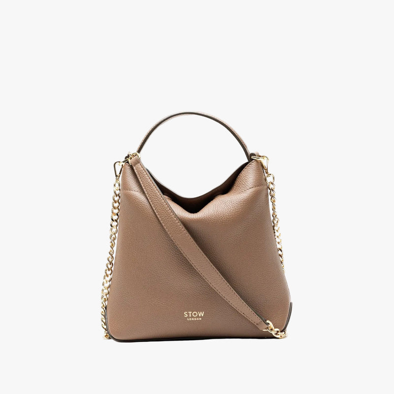 STOW London's Mini Curve in Mocha pebbled leather styled as a flap bag featuring gold-coated stainless steel hardware and chain strap on a light grey background