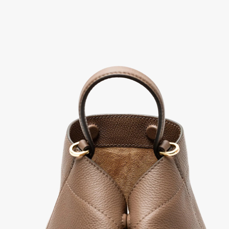 Close up of the handle on STOW London's Mini Curve in Mocha pebbled leather featuring gold-coated stainless steel hardware and hidden magnetic closures on a light grey background