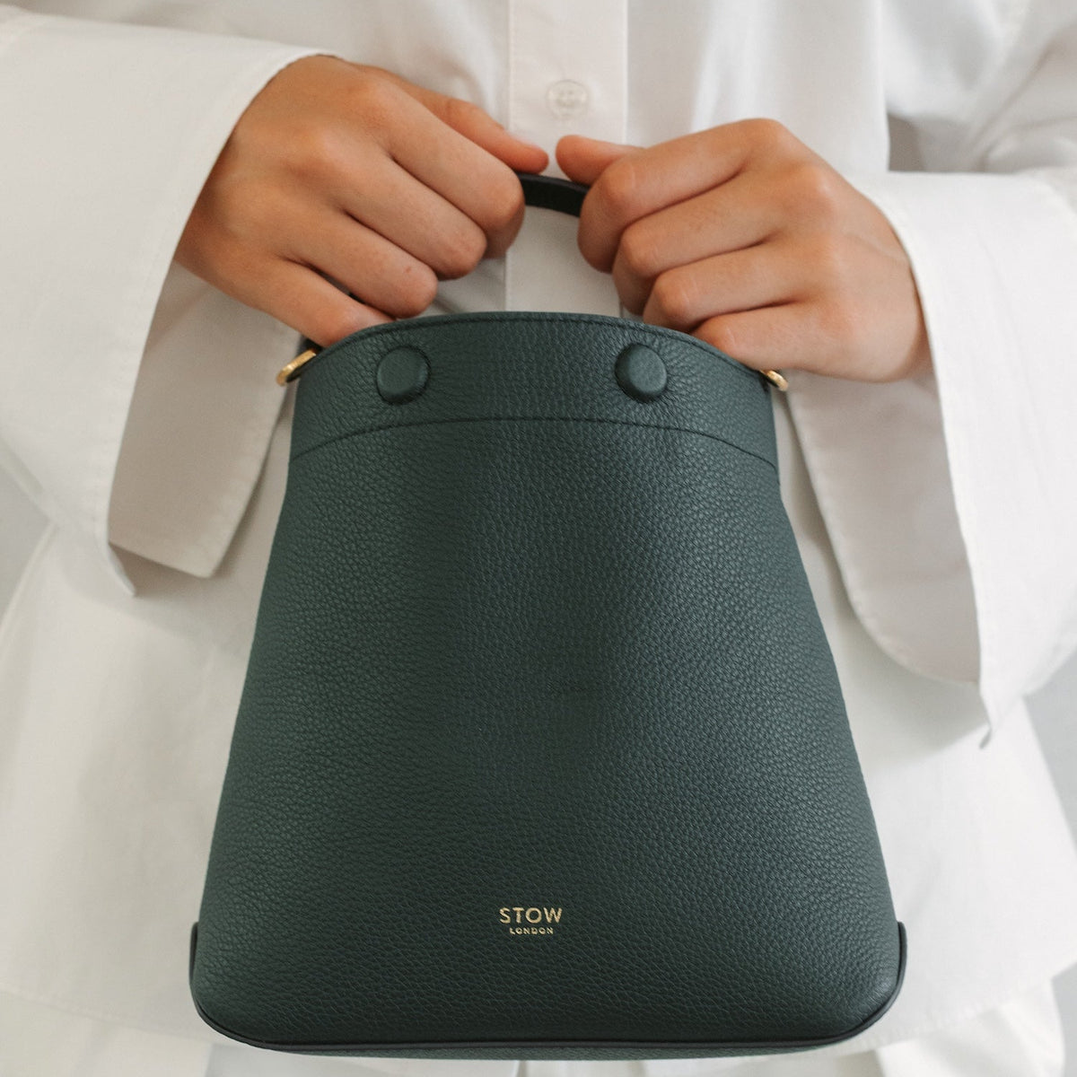 Model in a full white outfit holding STOW London's Mini Curve in New Forest pebbled leather featuring gold-coated stainless steel hardware and embossed logo