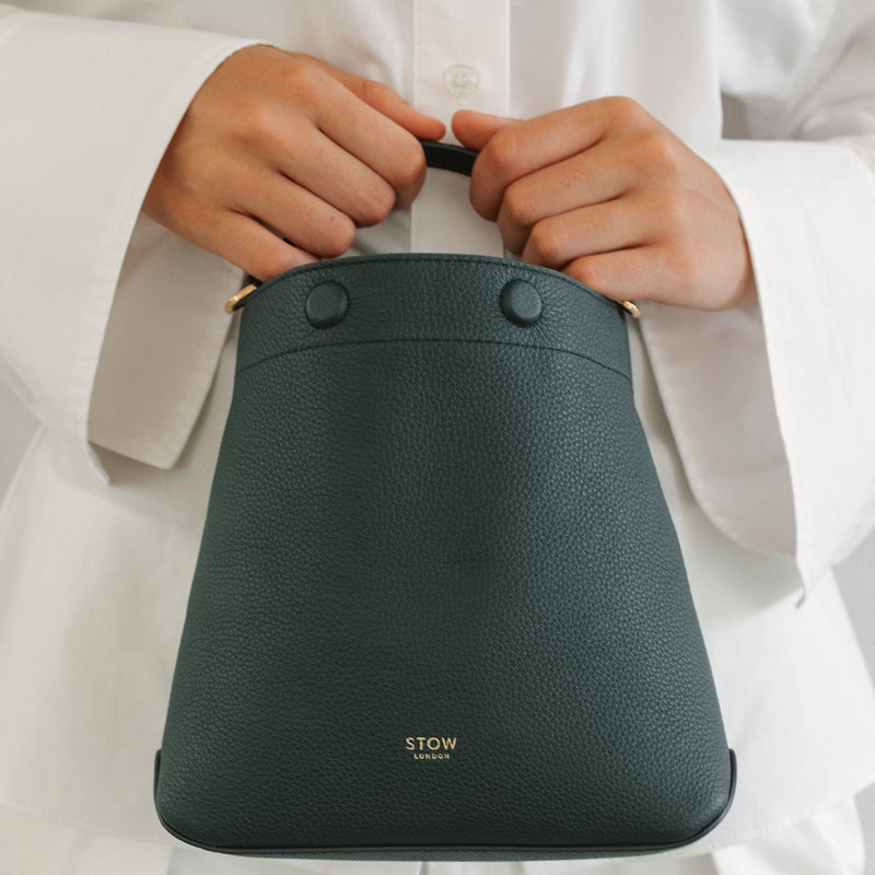 Model in a full white outfit holding STOW London's Mini Curve in New Forest pebbled leather featuring gold-coated stainless steel hardware and embossed logo