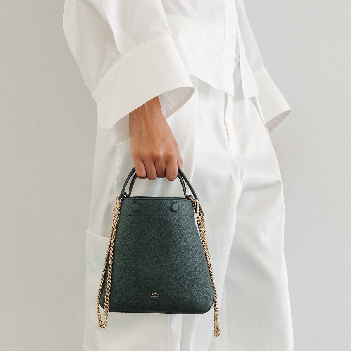Model in a full white outfit holding STOW London's Mini Curve in New Forest pebbled leather featuring the gold plated chain strap