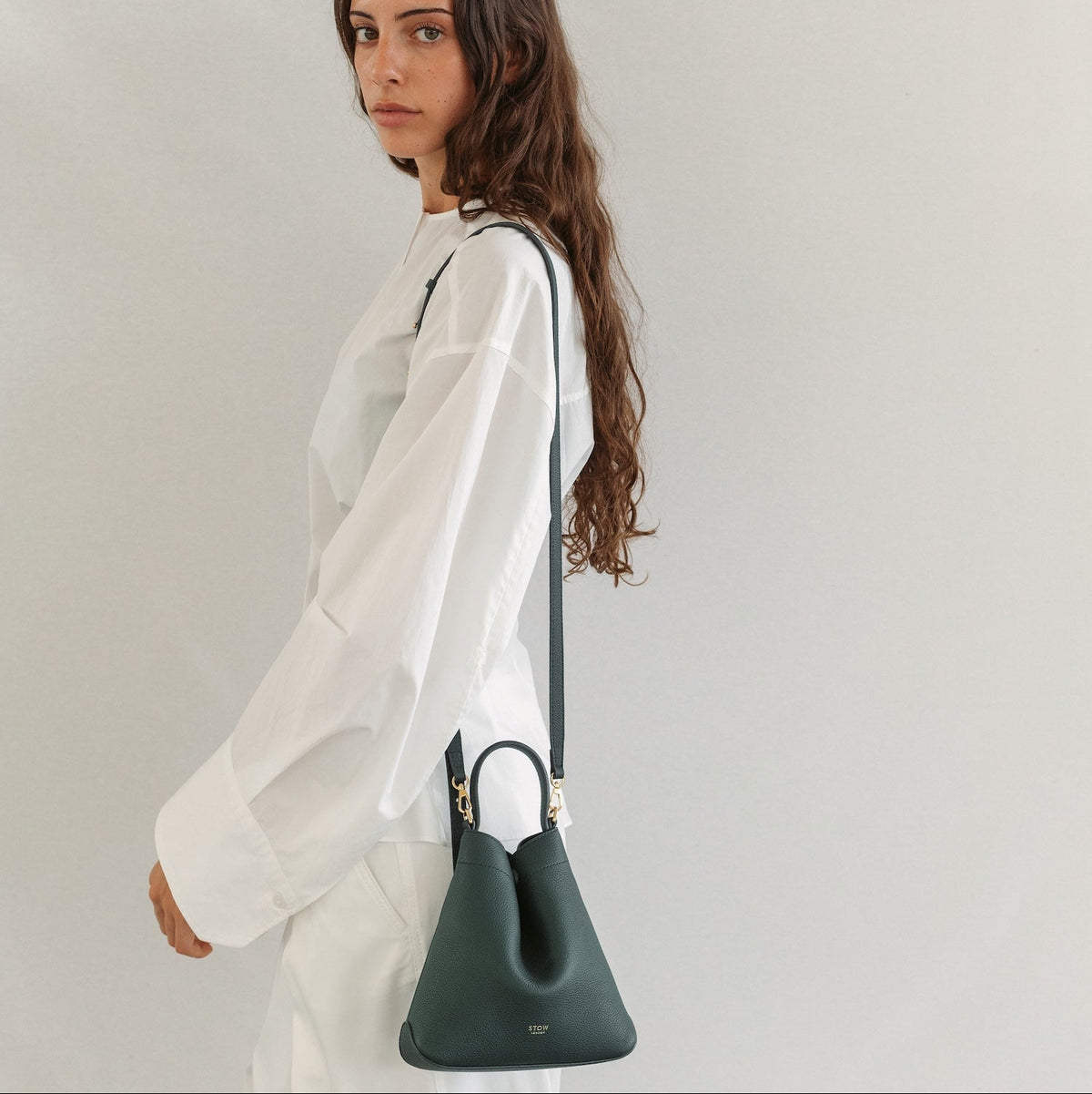 Model wearing STOW London's Mini Curve in New Forest pebbled leather on her shoulder featuring the detachable crossbody strap and gold-coated stainless steel hardware 