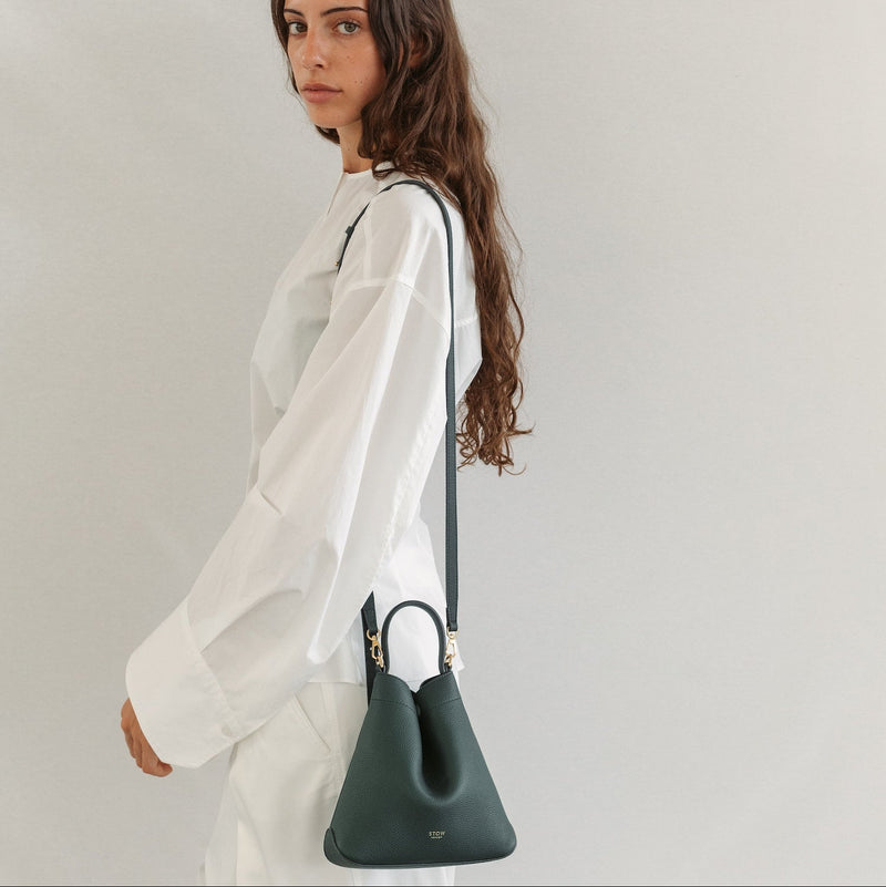Model wearing STOW London's Mini Curve in New Forest pebbled leather on her shoulder featuring the detachable crossbody strap and gold-coated stainless steel hardware 