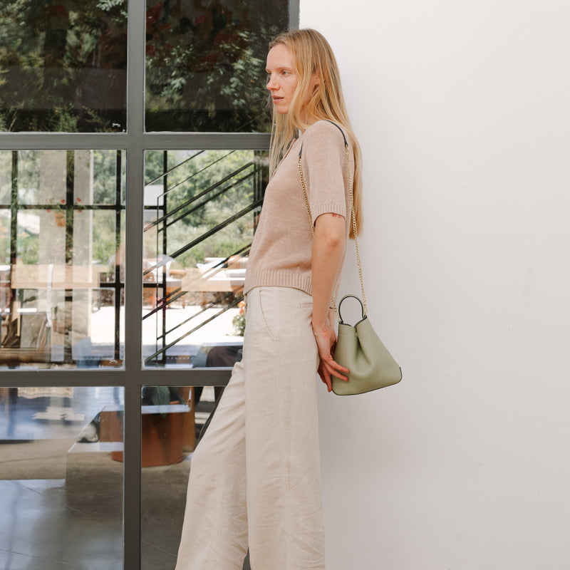 Model wearing STOW London's Mini Curve in Pale Green pebbled leather featuring a gold chain strap. 